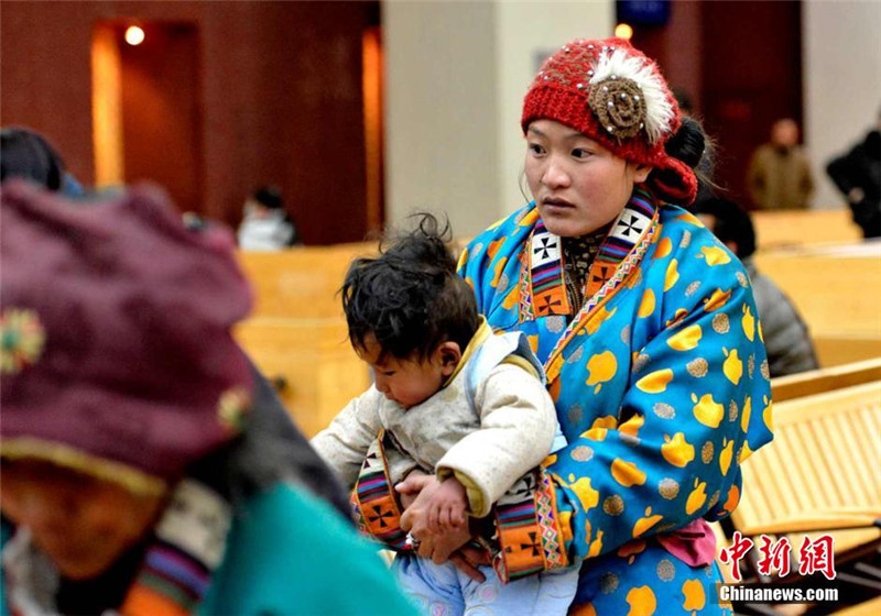 2月4日，身着特色民族服装的藏族妇女怀抱孩子在拉萨火车站候车大厅排队等候。李林 摄