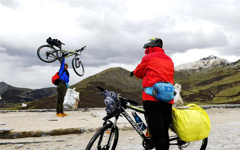 骑行川藏公路的一名车友在西藏米拉山口举起自行车让同伴拍照（6月14日摄）。