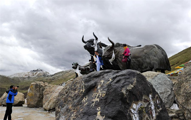 游人在西藏米拉山口藏耗牛石雕像前拍照留影（6月14日摄）。
