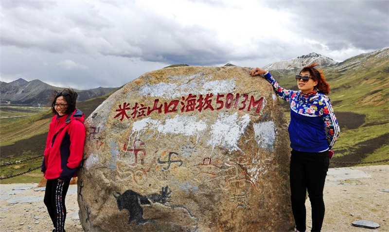 游人在西藏米拉山口刻有海拔高度的巨石前留影（6月14日摄）。