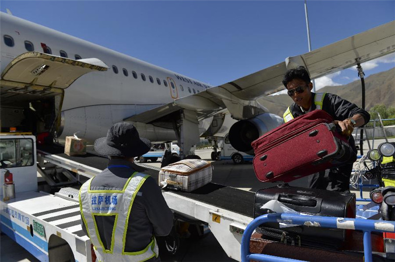 6月30日，西藏拉萨贡嘎机场的工作人员在搬运乘客托运的行李。