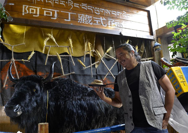 巴桑次仁在“阿可丁藏式面包坊”门口的牦牛模型前展示黑青稞“牛粪面包”（7月9日摄）。