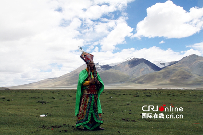 在雪山前的草地上，布琼正表演藏族史诗《格萨尔王传》的第一回《赛马称王》。摄影：付承堃
