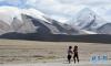 8月21日，两名藏族儿童在昆仑山下玩耍，远处是昆仑山东段最高峰玉珠峰。初秋时节的昆仑山白雪皑皑，矗立在云间的玉珠峰高大雄伟，银装素裹。玉珠峰又称可可赛极门峰，海拔6178米，是昆仑山东段的最高峰。新华社记者李晓果摄